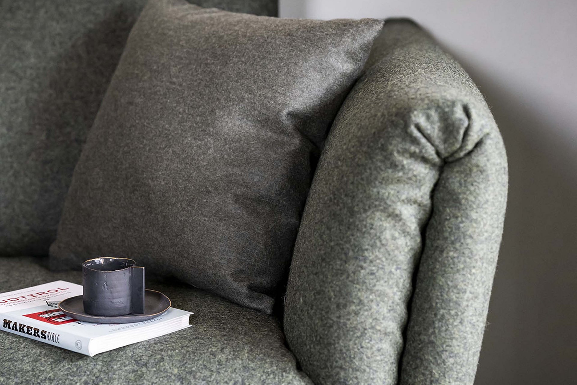 Urlaub mit Stil in der Residence Alma Paramout Graues Stoffsofa mit Kissen und Buch mit Tasse auf der Armlehne