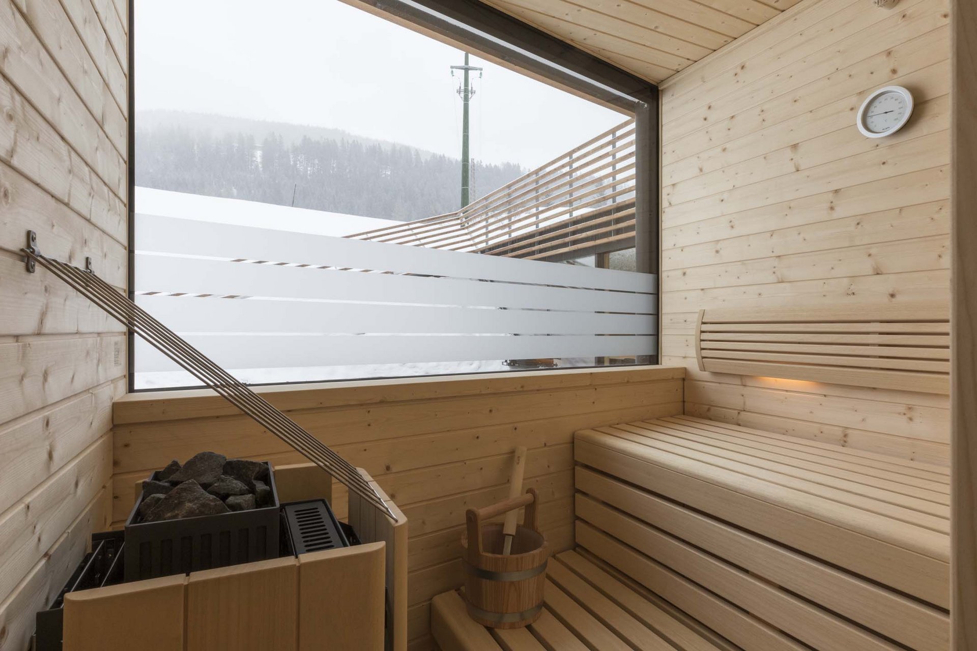 Urlaub mit Stil in der Residence Alma Paramout Sauna mit Holzinterieur und Fensterblick auf verschneite Berge