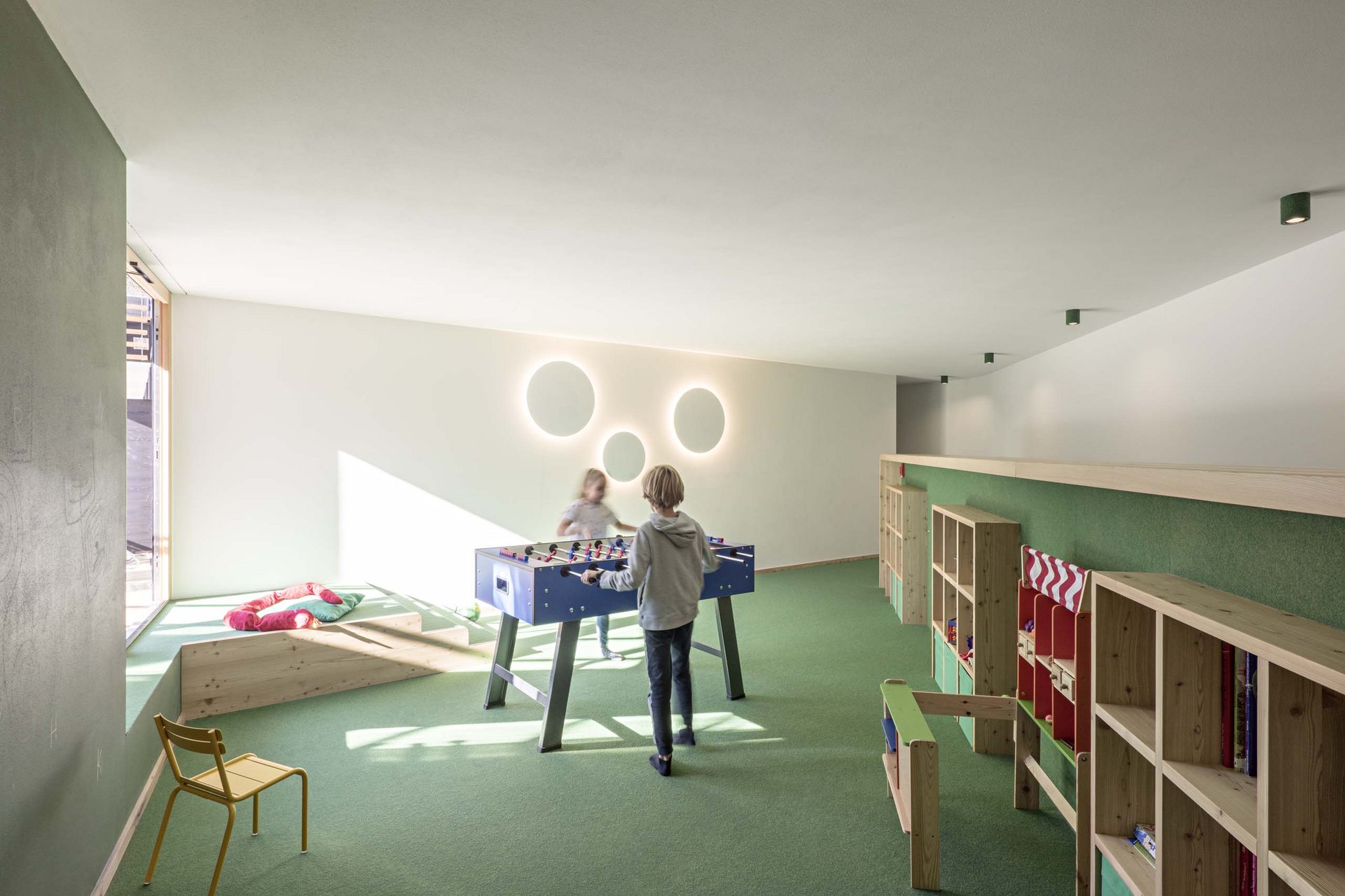 Urlaub mit Stil in der Residence Alma Paramout Kinder spielen Tischfußball in einem hellen, modernen Spielzimmer mit grütem Teppich