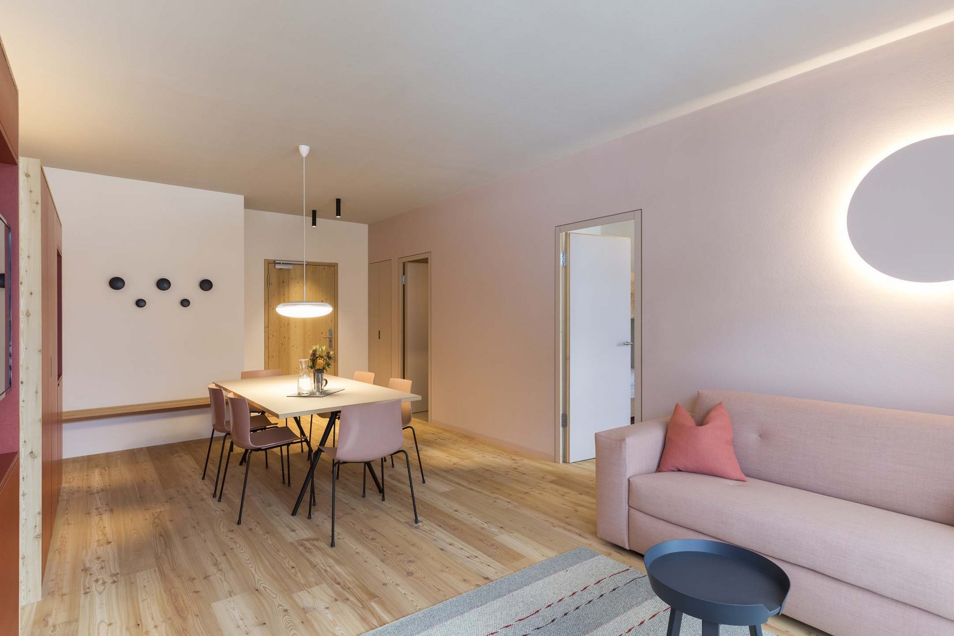 Urlaub mit Stil in der Residence Alma Paramout Modernes Wohnzimmer mit Esstisch, rosa Sofa und runder Wandlampe