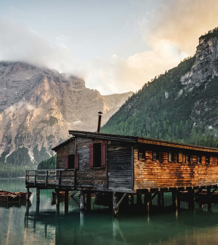 Sights around Sexten Wooden house on stilts by lake with mountains and boats in mist