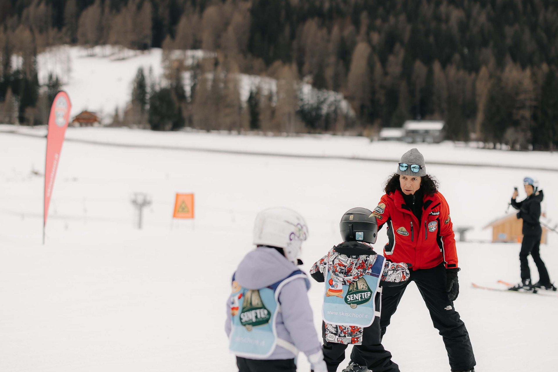 The in-house Rainer Ski School Ski instructor teaching children skiing on snowy slope with forested mountain