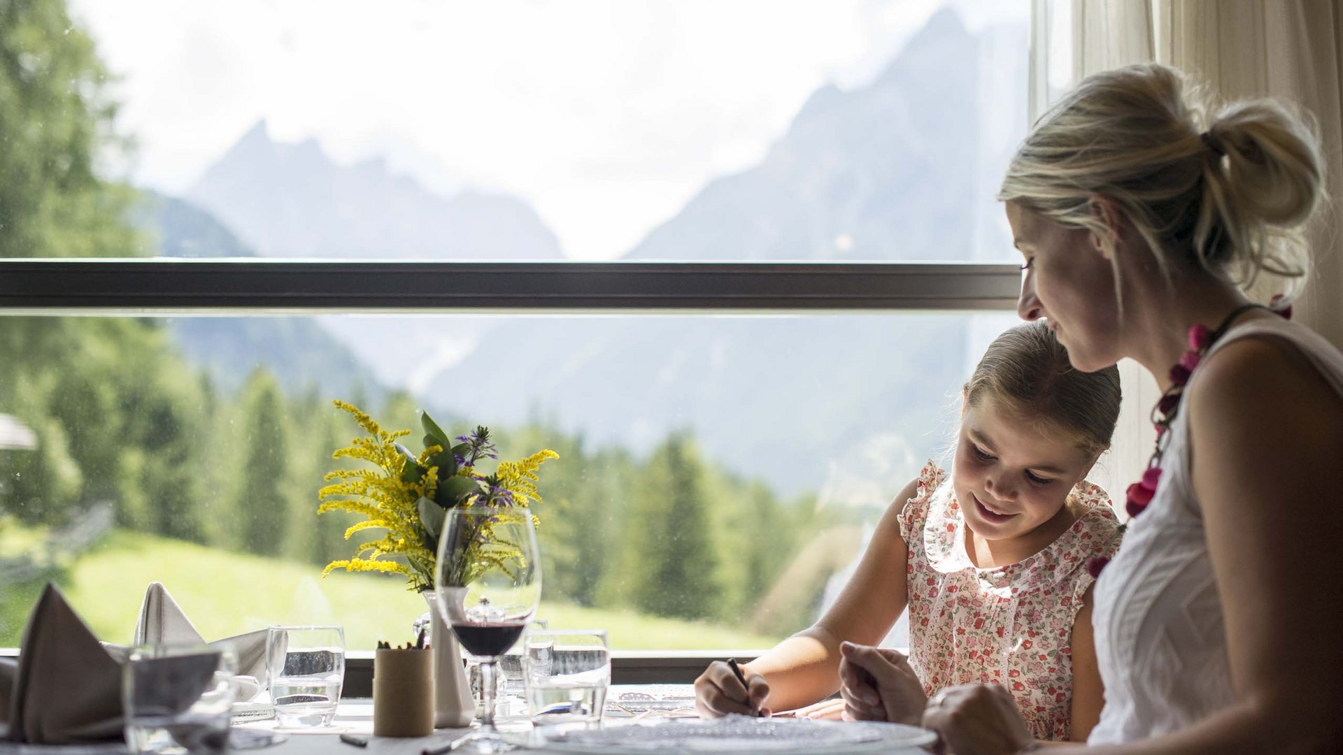 Family Resort Rainer Donna e bambina disegnano al tavolo con vista sulle montagne