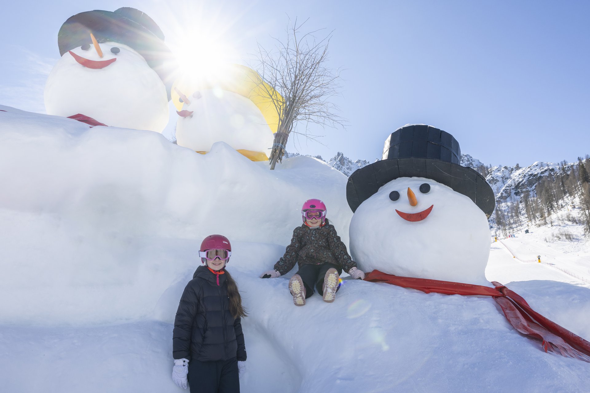 Il vostro family resort in Alto Adige Due bambini in abiti invernali accanto a grandi pupazzi di neve tra le montagne