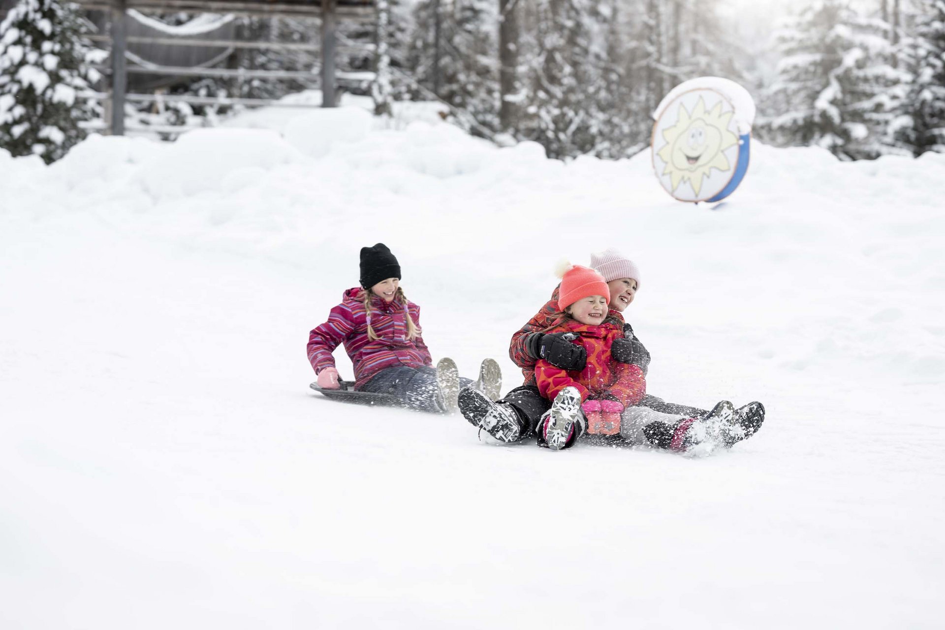 Ihr Familienresort in Südtirol Drei Kinder rodeln gemeinsam im verschneiten Winterwald.