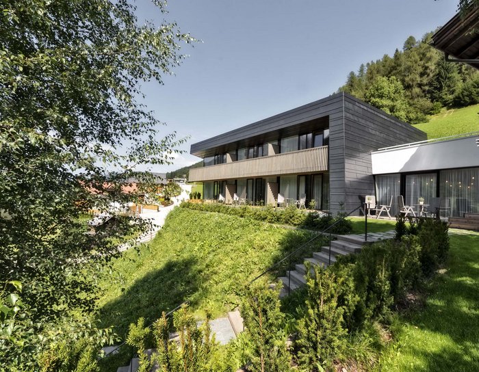 Ihr Familienresort in Südtirol Modernes Gebäude in grüner Hügellandschaft bei sonnigem Himmel