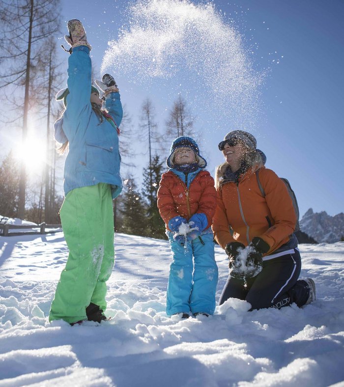 Ihr Familienresort in Südtirol Familie spielt im Schnee bei sonnigem Wintertag im Wald