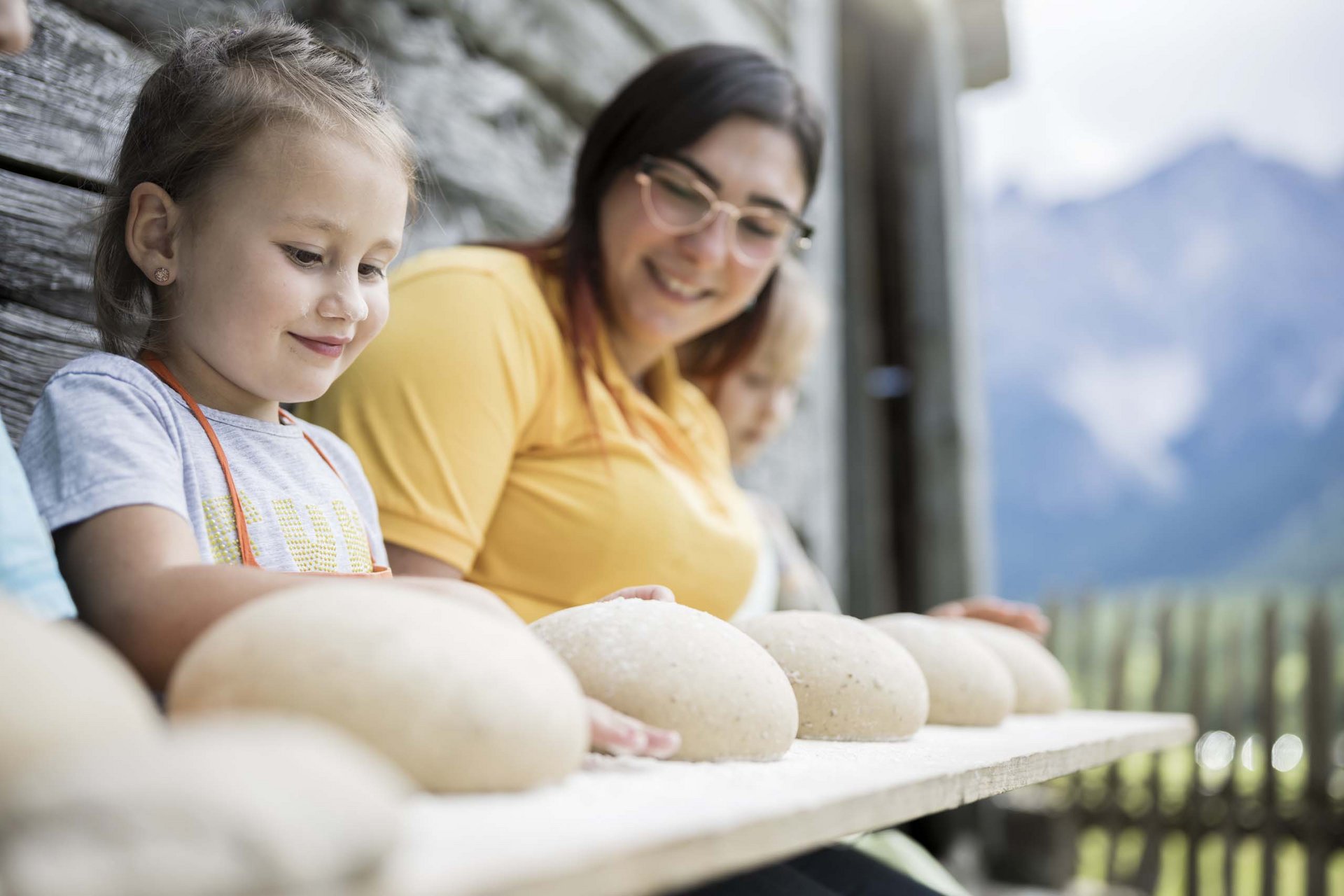 Ihr Familienresort in Südtirol Kind und Erwachsene formen Brotteigbälle auf einem Holzbrett draußen