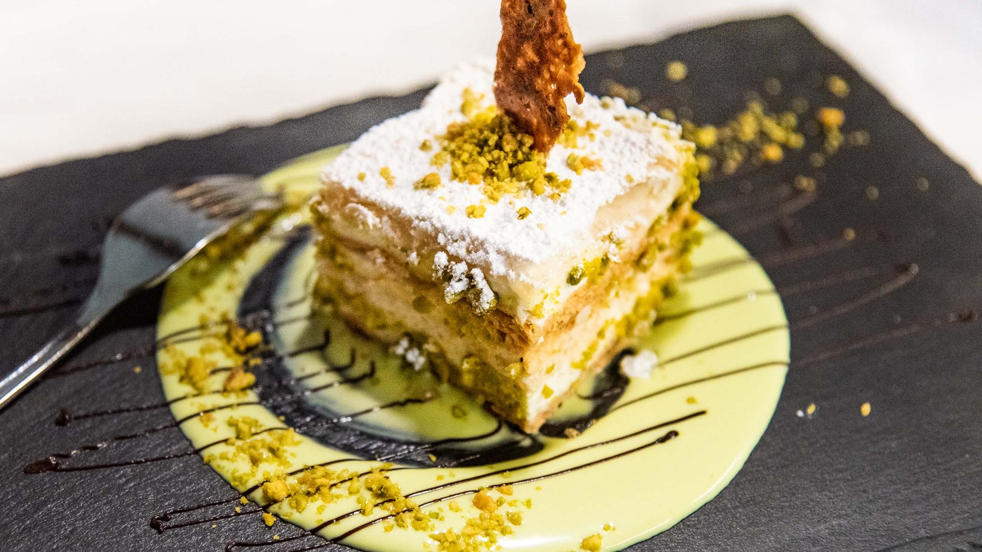 Family Resort Rainer Fetta di tiramisù con pistacchi e zucchero a velo su piatto nero