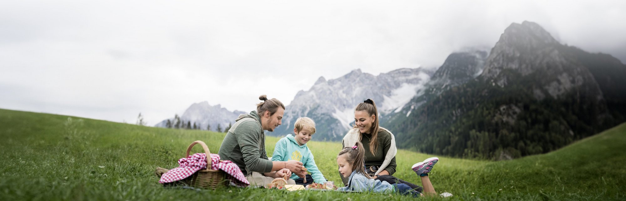 Famiglia fa un picnic su un prato verde con montagne sullo sfondo