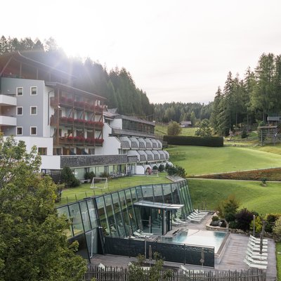 Hotelgebäude mit Balkon und großem Rasen vor Berglandschaft unter blauem Himmel