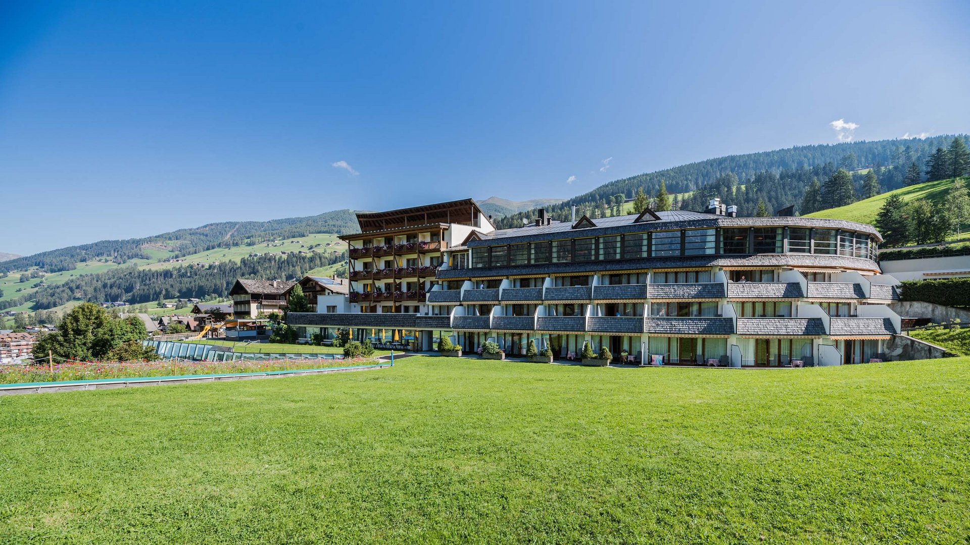 Your fulfilling family holiday Hotel building with balconies and large lawn in front of green hills under blue sky