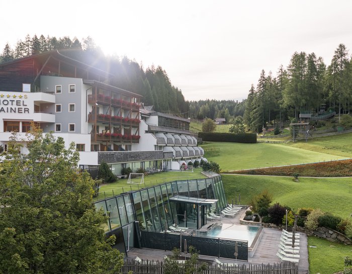 Hotelgebäude mit Balkon und großem Rasen vor Berglandschaft unter blauem Himmel