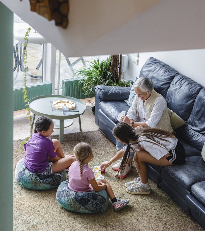 Drei Frauen und ein Mädchen spielen mit Karten im Wohnzimmer, während eine ältere Frau zusieht