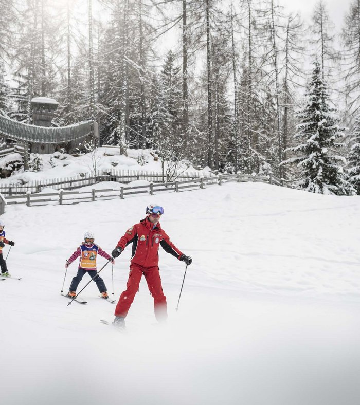 Il vostro family resort in Alto Adige Istruttore di sci insegna a due bambini a sciare in una foresta innevata