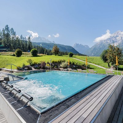 Relaxing wellness in the Dolomites: spa hotel in Sexten Outdoor pool with jacuzzi and mountain view in summer