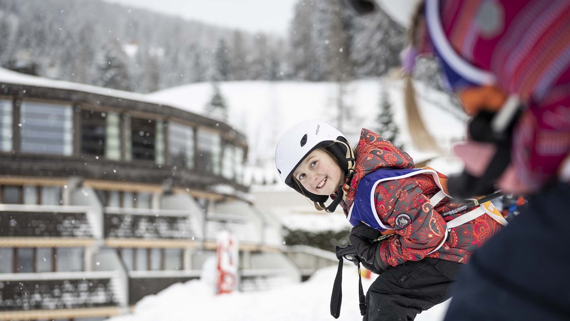 Your fulfilling family holiday Smiling child with helmet skiing in snow near a building