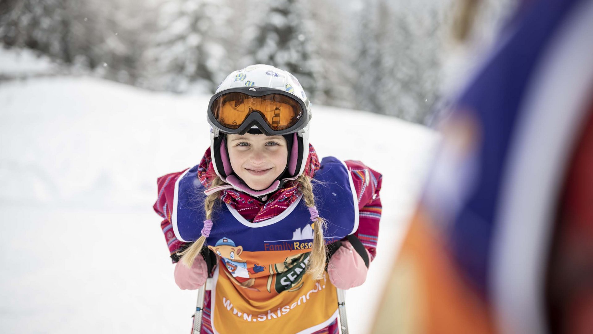 Your hotel with childcare in the Dolomites Girl in ski gear smiling during a snowy ski lesson