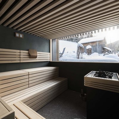 Relaxing wellness in the Dolomites: spa hotel in Sexten Modern sauna interior with wooden bench and snowy cabin view outside