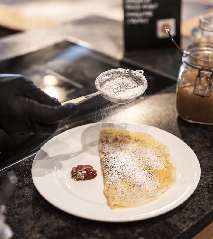 Family holidays at a gluten-free hotel Crepe being dusted with powdered sugar next to a strawberry on a white plate.