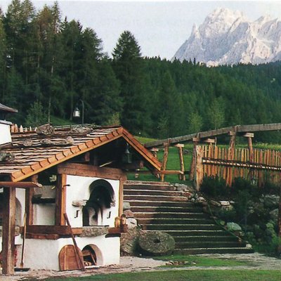 Vecchia casa in legno con forno a legna e bosco davanti a montagne