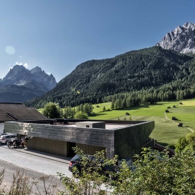 Ihr Familienresort in Südtirol Haus und moderne Gebäude vor grünen Wiesen und gezackten Bergen bei klarem Himmel