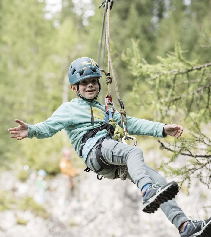Family Resort Rainer: your accommodation in the Dolomites Happy boy wearing helmet climbing on rope in the forest