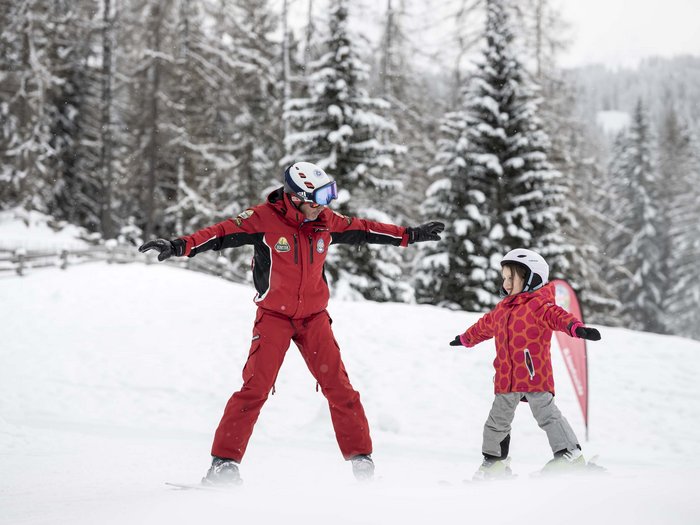 Ski instructor teaching child in red jacket to ski in the snow