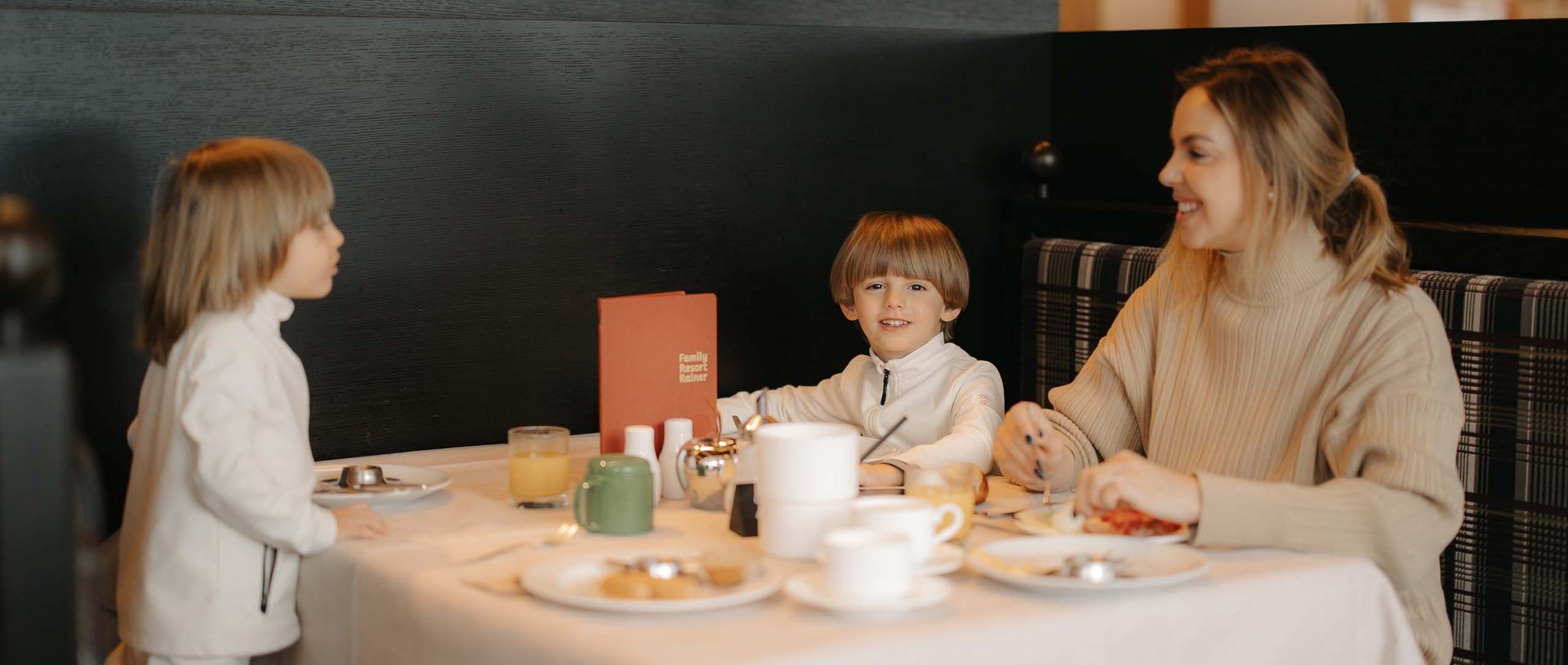 Stay at the Rainer: Family holidays in the Dolomites! Woman and two children having breakfast in a restaurant