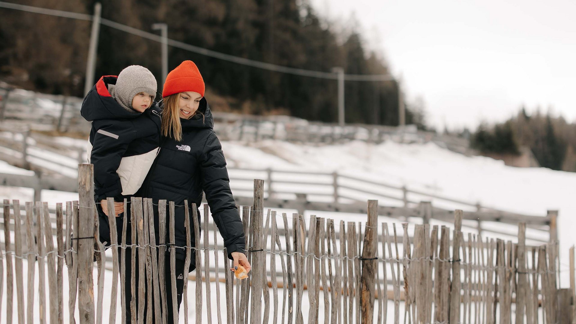 Qualche immagine del Rainer Donna e bambino danno da mangiare alle galline nella neve dietro una staccionata
