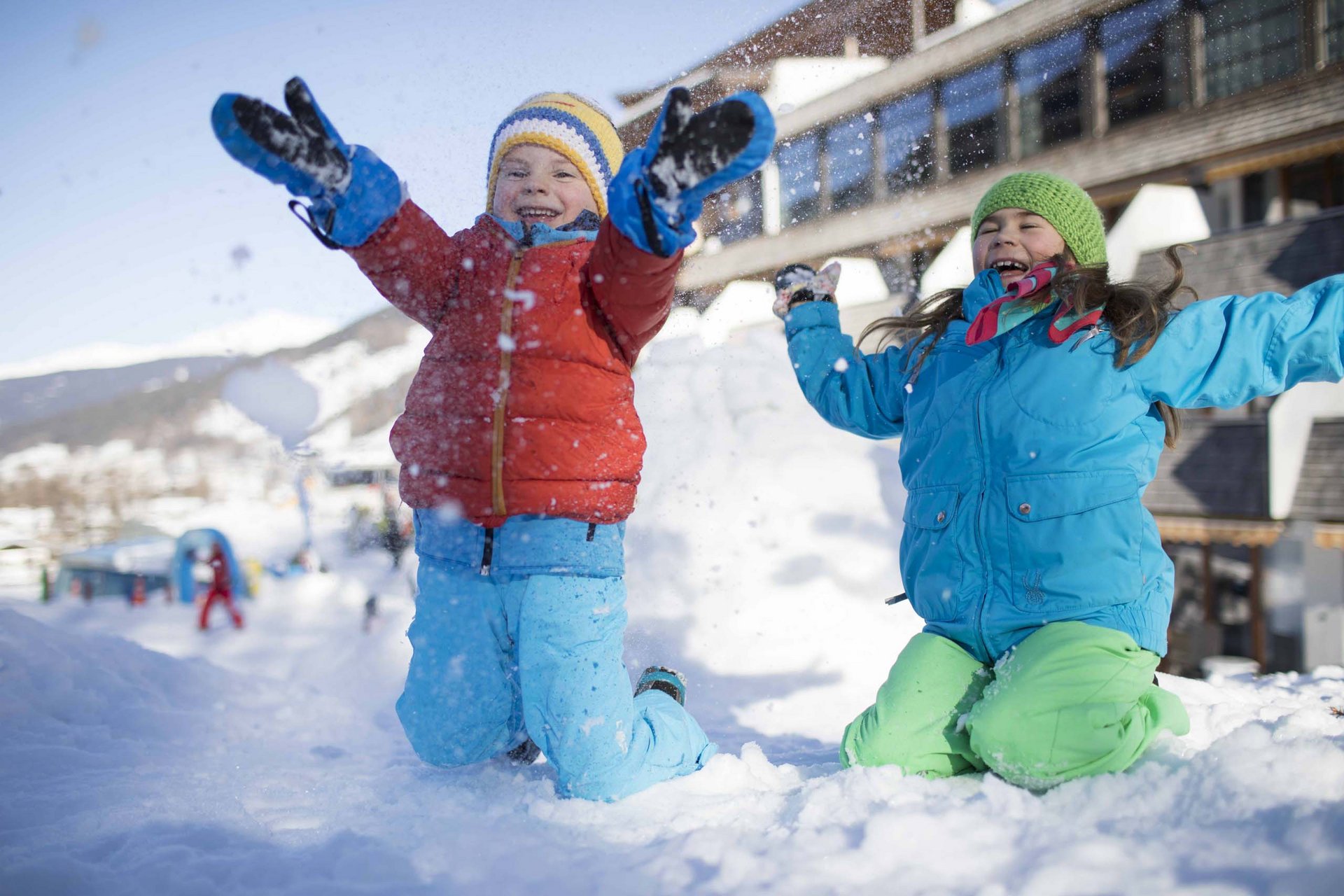 Ihr Familienresort in Südtirol Zwei Kinder spielen lachend im Schnee vor einem Gebäude