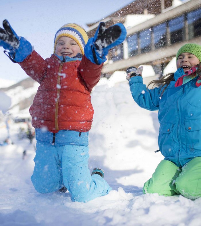 Your fulfilling family holiday Two children happily playing in the snow in front of a building