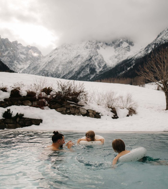 Ihr Familienresort in Südtirol Vater und Kinder schwimmen im Pool vor verschneiten Bergen