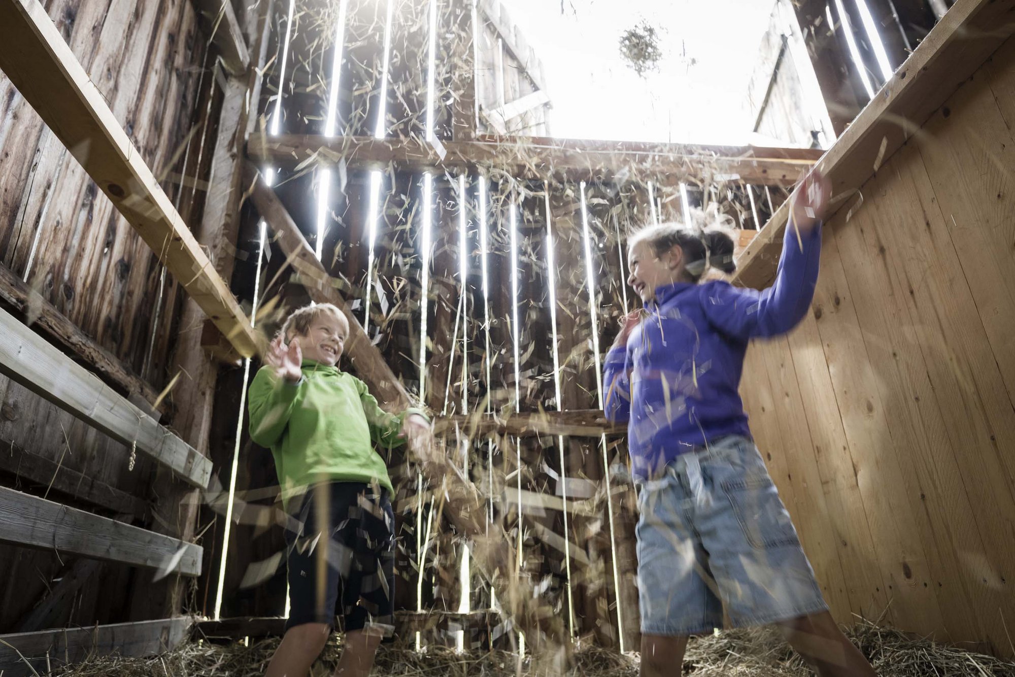 Our family experiences Two children laughing and playing with hay in a barn