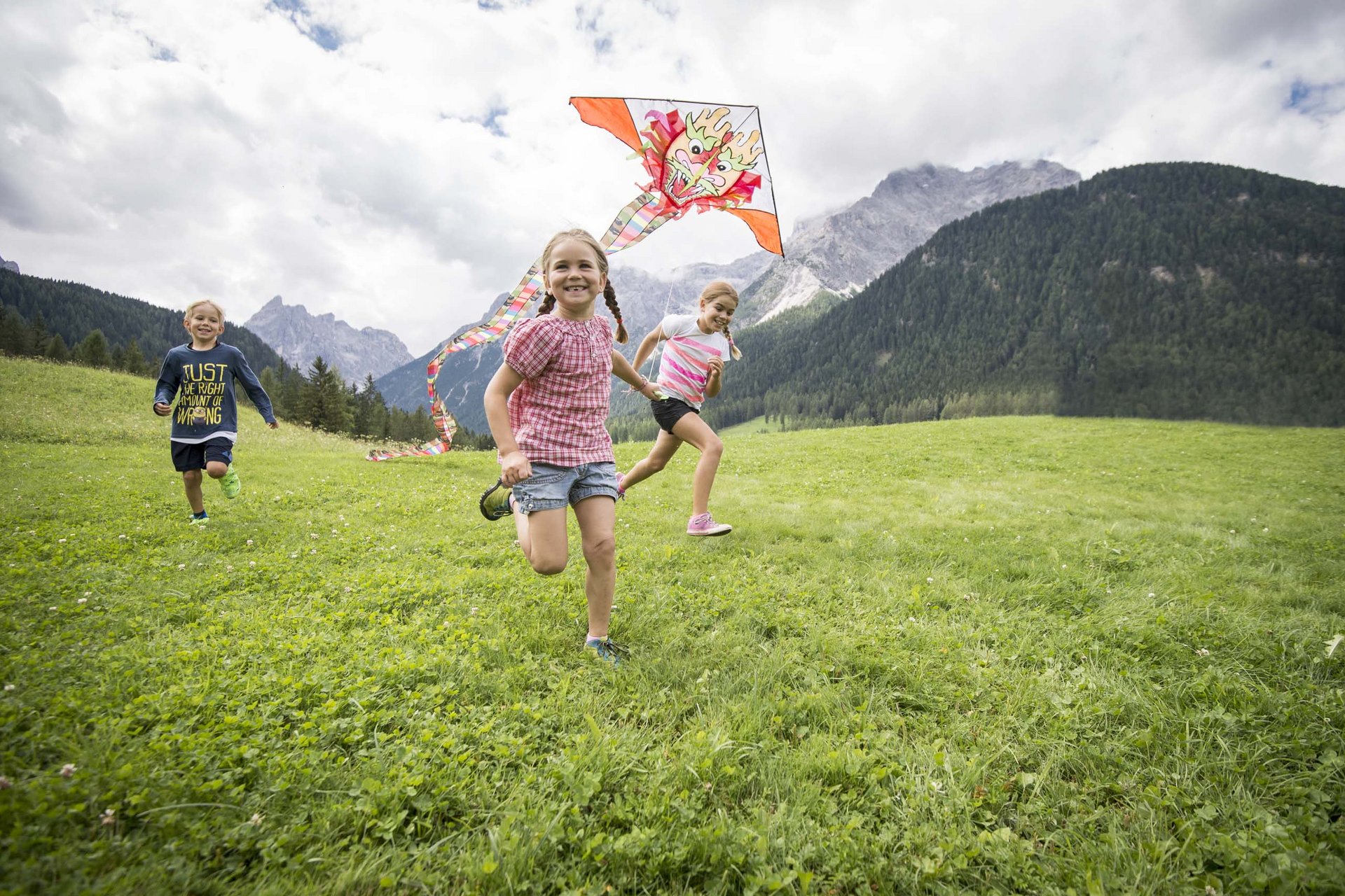 Ihr Familienresort in Südtirol Kinder rennen auf einer Wiese und lassen einen Drachen mit Drachenkopf fliegen