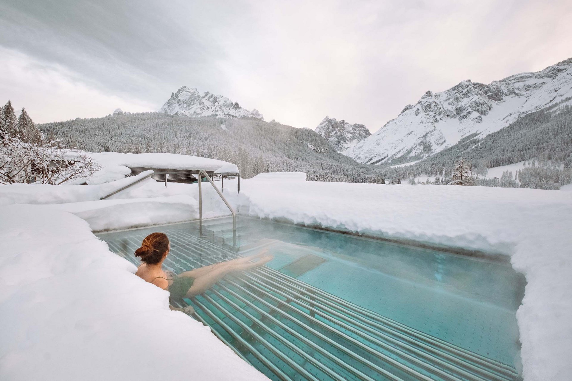 How to get to the Family Resort Rainer Woman relaxing in heated outdoor pool surrounded by snowy mountains