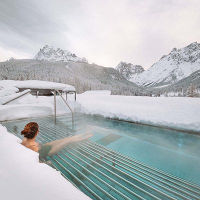 Relaxing wellness in the Dolomites: spa hotel in Sexten Woman relaxing in heated outdoor pool surrounded by snowy mountains