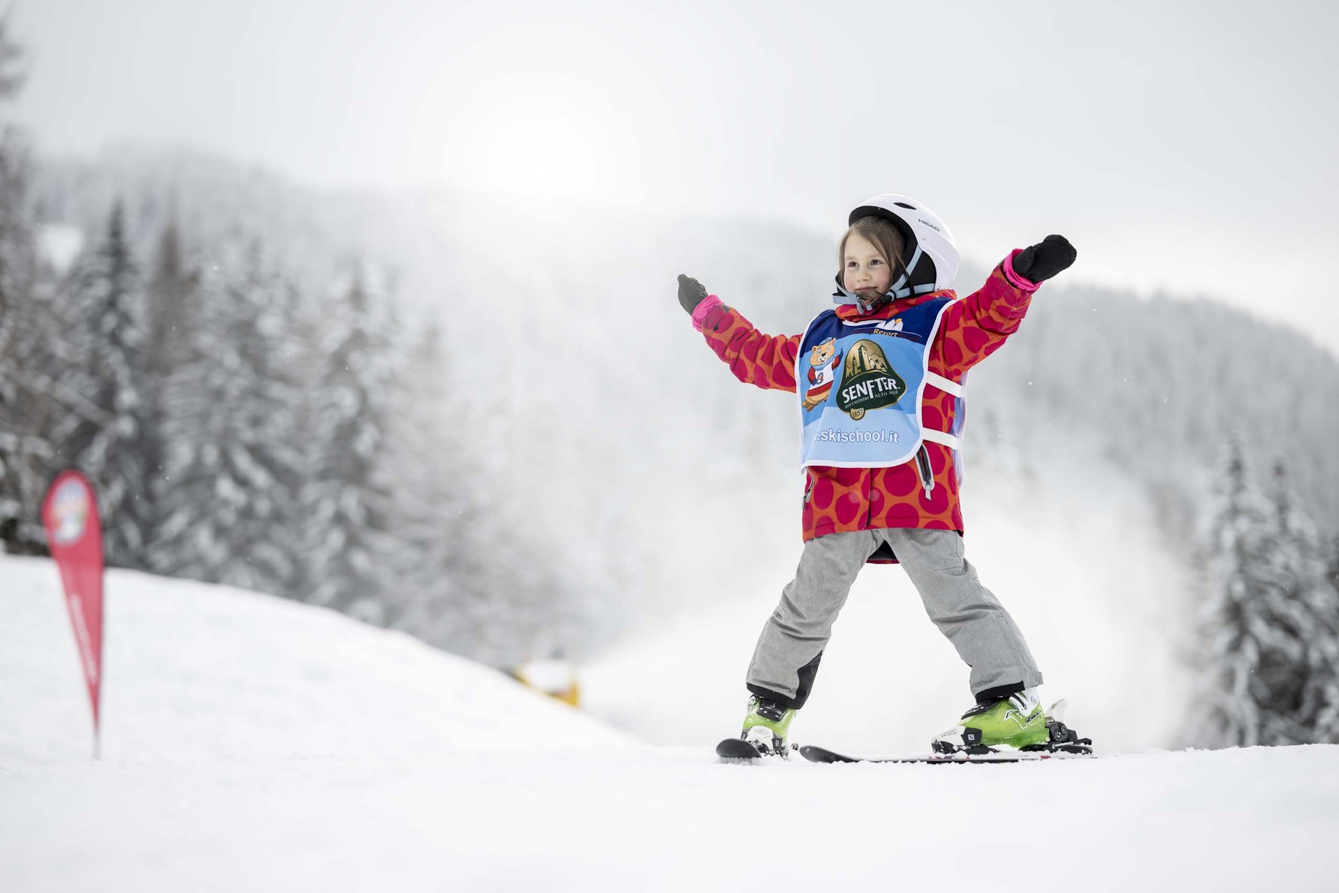 How to get to the Family Resort Rainer Child in ski helmet and red jacket skiing on snow with arms stretched out
