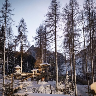 Parco giochi innevato con strutture in legno e scivoli in una foresta invernale