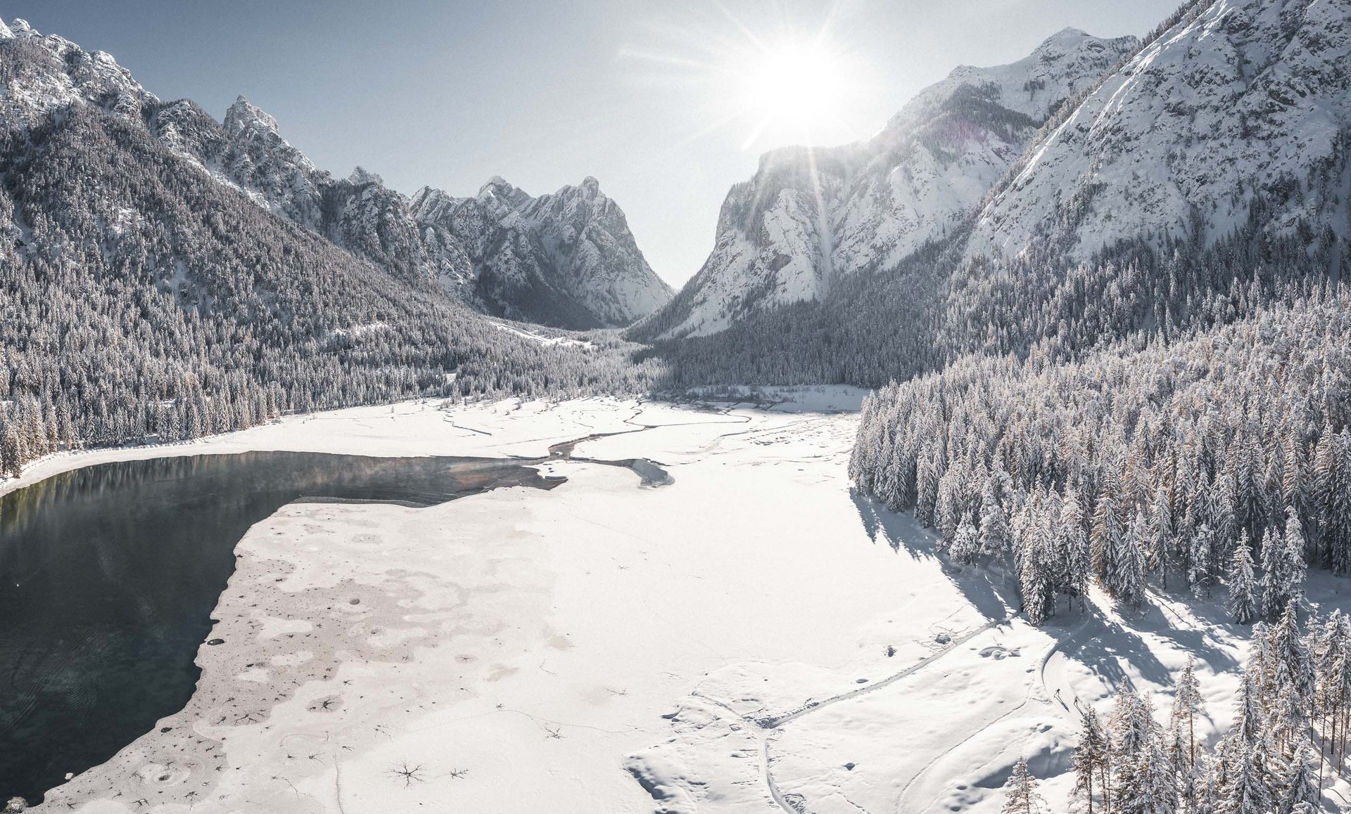 Montagne innevate e foresta con lago parzialmente ghiacciato al sole