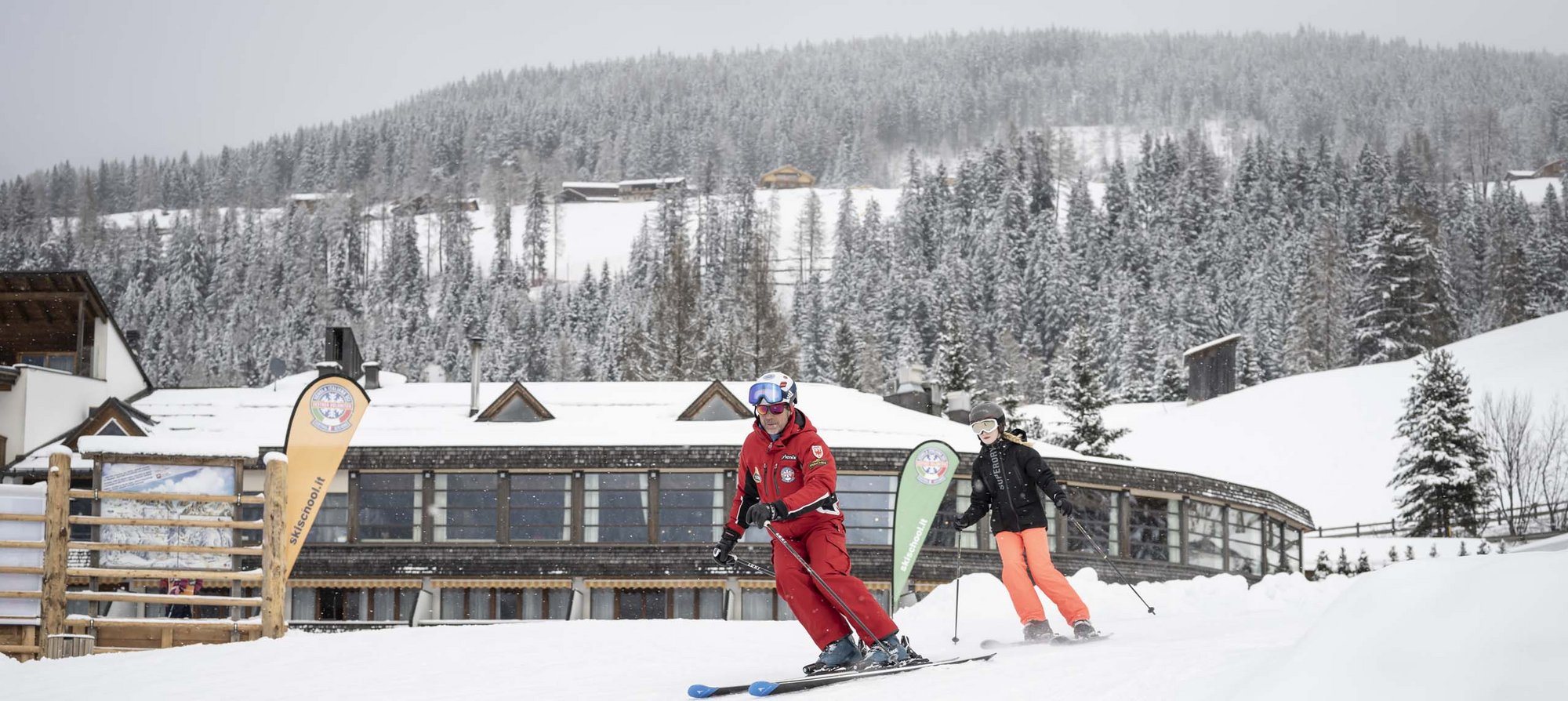 Your fulfilling family holiday Ski instructor teaching a student on snow-covered slope in front of mountain lodge