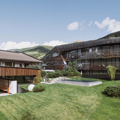 Ihr Familienresort in Südtirol Moderne Gebäude mit Garten und Bergen im Hintergrund an einem sonnigen Tag