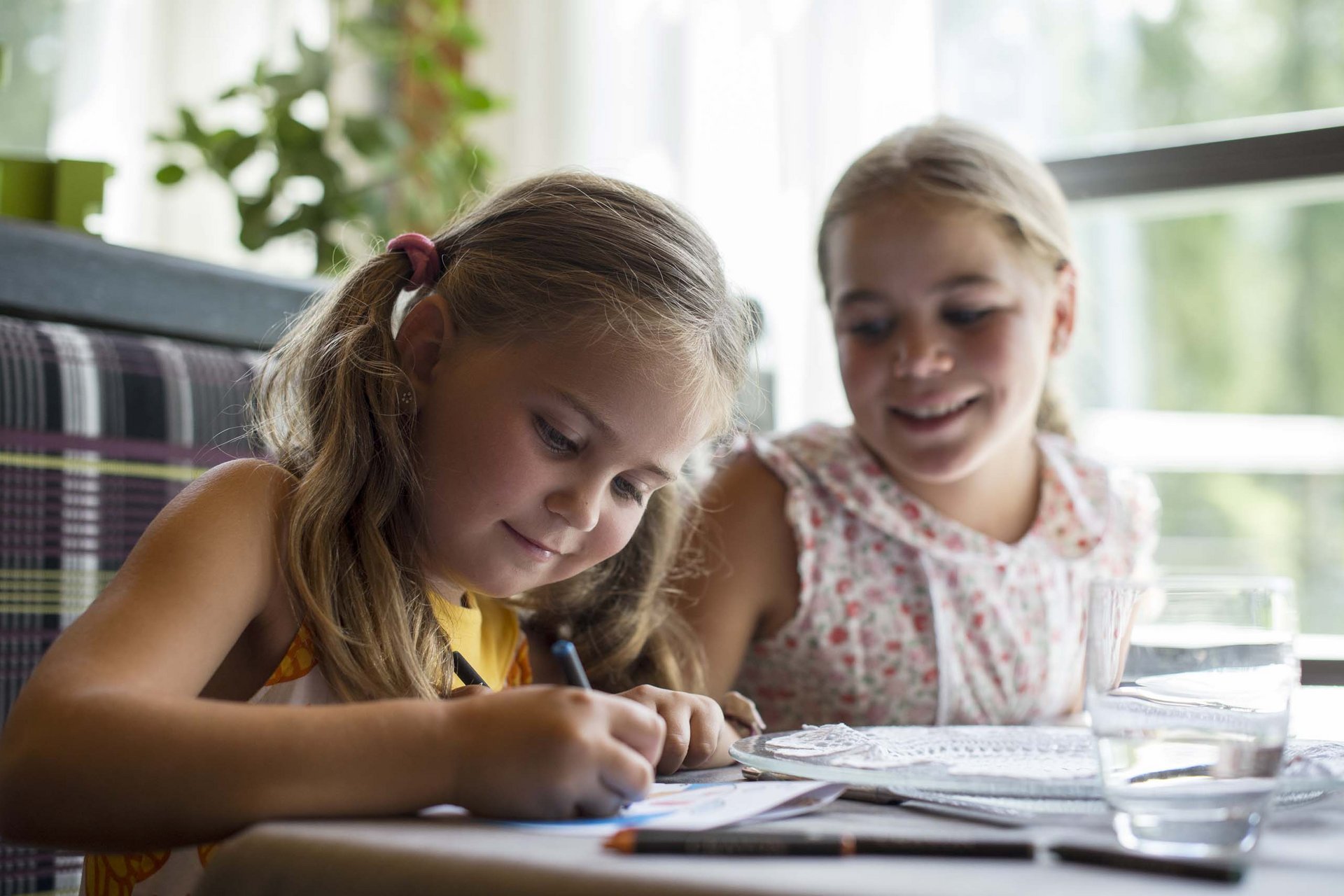 Due ragazze sedute a tavola, una disegna concentrata