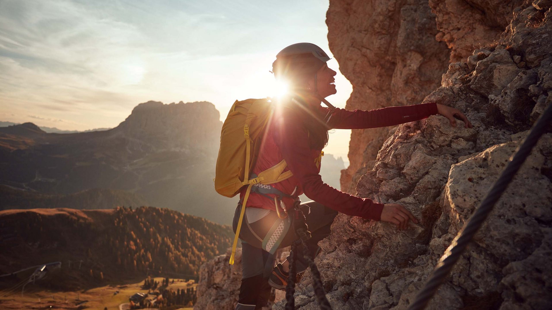 Qualche immagine del Rainer Donna che scala una parete rocciosa con casco e zaino al tramonto