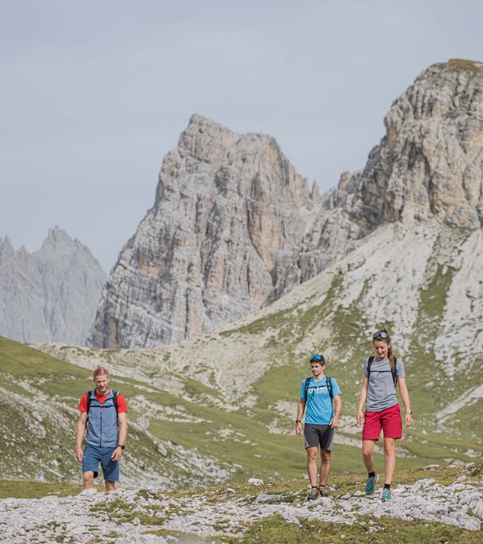 Stay at the Rainer: Family holidays in the Dolomites! Three hikers on a mountain trail with rocky peaks in the background