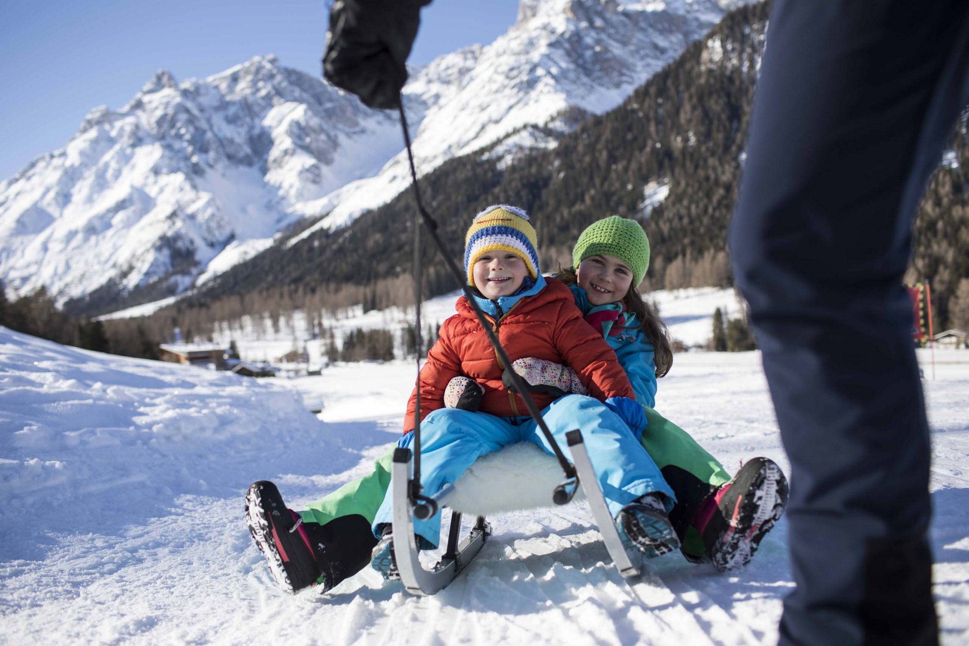 Ihr Familienresort in Südtirol Zwei lachende Kinder auf einem Schlitten im Schnee vor verschneiten Bergen