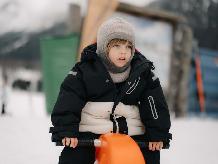 Your hotel with childcare in the Dolomites Child in winter outfit sitting on orange play equipment in the snow