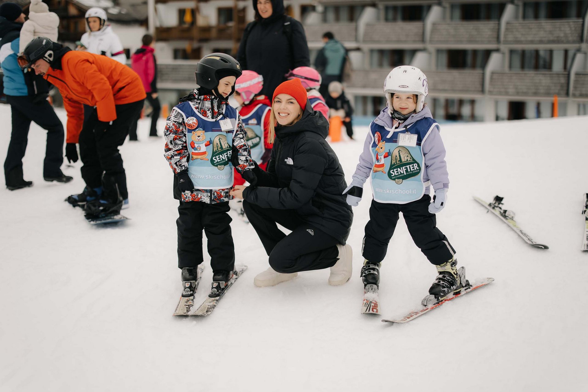 Ihr Familienresort in Südtirol Kinder lernen Skifahren mit einer Lehrerin auf einem schneebedeckten Hang