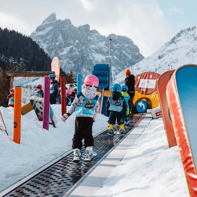 Ihr Familienresort in Südtirol Kinder lernen Skifahren auf einem Förderband im Ski-Kinderpark mit Bergkulisse