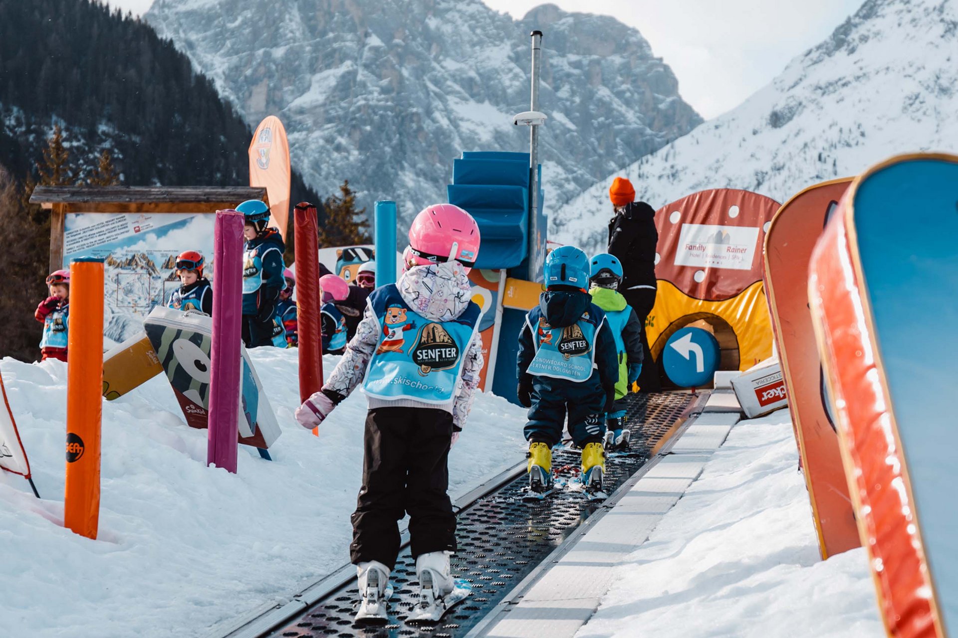 The in-house Rainer Ski School Children learning to ski on a conveyor belt in a ski kids park with mountain background